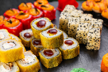 sushi rolls laid out on a dark background decorated with bamboo leaves and chopsticks