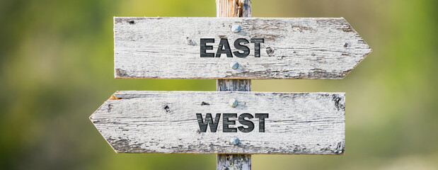 opposite signs on wooden signpost with the text quote east west engraved. Web banner format. © Jon Anders Wiken