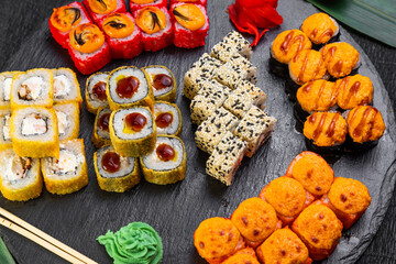 sushi rolls laid out on a dark background decorated with bamboo leaves and chopsticks