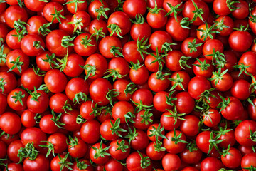 Background of round ripe small cherry tomatoes with green ponytails
