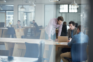 Hes got a lot of experience to offer the team. Shot of a group of colleagues talking together over a laptop in an office.