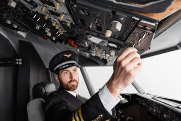 pilot in cap and uniform reaching overhead panel in airplane simulator.