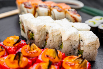 sushi rolls laid out on a dark background decorated with bamboo leaves and chopsticks