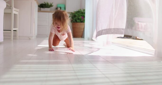 a toddler baby girl crawling on the floor at home with curtains swaying on the summer breeze
