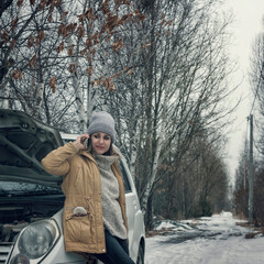 The girl is alone on the snowy road. The car broke down, the hood is open. Frustrated woman calls on the phone, calls technical support.