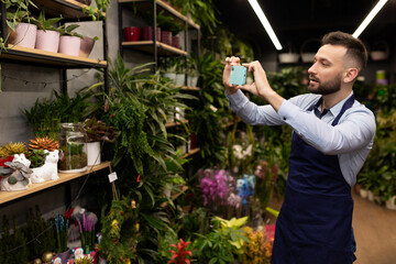 a garden center worker takes a picture of a display case with potted plants on his phone