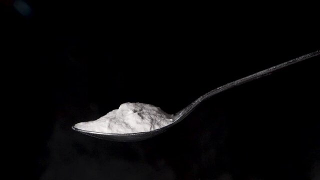 Blowing away flour powder from a spoon in slow motion, isolated black background