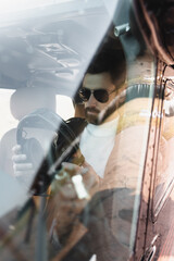 view of bearded pilot in stylish sunglasses holding headphones in cockpit through helicopter windscreen. © LIGHTFIELD STUDIOS