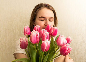 Womans day concept: Young woman holds pack of tulips near her face while enjoying herself