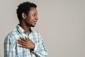 Black unshaven man holding hand on his chest while looking aside