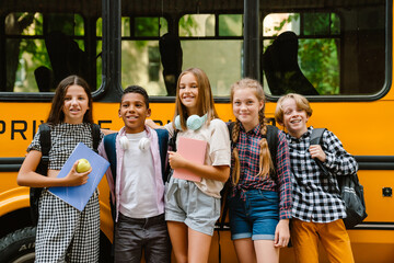 Multiracial pupils smiling while standing by school bus