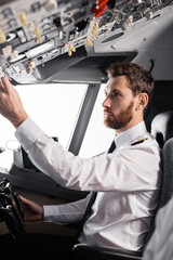 Fototapeta na wymiar bearded pilot reaching overhead panel while using yoke in airplane simulator.
