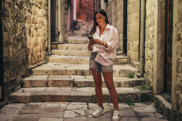 Beautiful young woman using smartphone while walking on the city streets on the coast during the night
