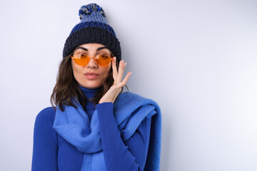 Young woman in a blue golf turtleneck, hat and scarf, sunglasses, on a white background, cheerful in a good mood