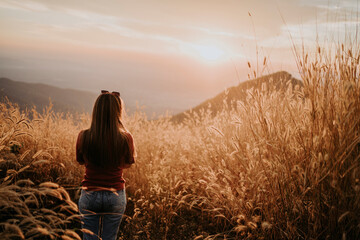 Fototapeta premium A beautiful Asian woman looks at the sunset in the grass in the warm light.