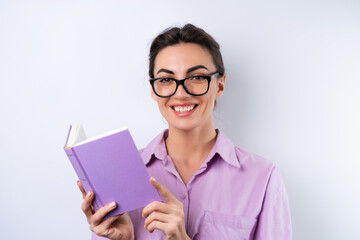 A young woman in a lilac shirt on a white background holds a book in her hands in glasses for vision