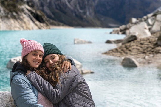 Two friends smiling while embracing in the shore of a lake