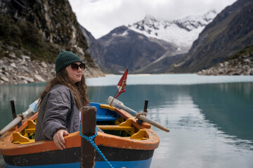 Young woman sitting in a wooden boat while gazing the landscape with a lake