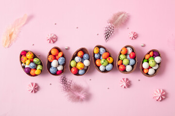 Fototapeta na wymiar Chocolate easter eggs and decor flat lay for kids easter hunt egg concept on pink background. Sweets in the shape of an egg