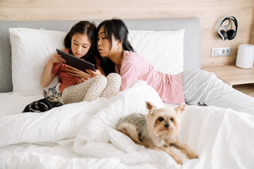 Asian mother and daughter using laptop while sitting on bed