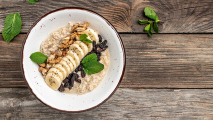 Oatmeal with dried raisins, banana and walnuts decorated with mint, Healthy diet vegetarian breakfast or snack, Clean eating, dieting, vegan food concept. top view