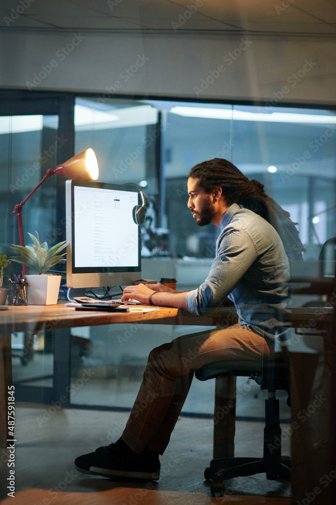 Aufkleber Putting in the hours to achieve success. Shot of a young designer working late on a computer in an office.