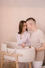 Stylish young family, photographed with a little beautiful baby. Family and parenting concept. Parents put the baby to sleep in a baby cradle