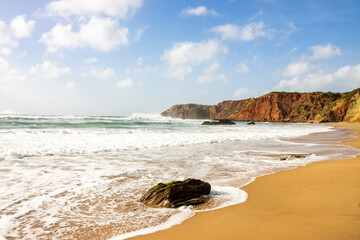Fototapeta na wymiar Beach with golden sand, clear water, blue sky and red cliffs in Algarve, Portugal