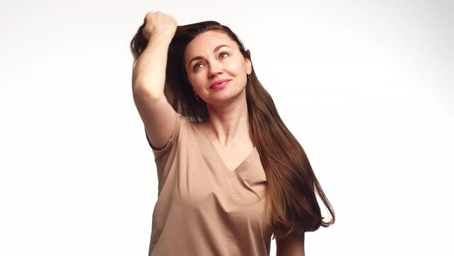 Attractive woman smile and combs hair with hand, going through them beautifully, front view. Woman long brown hair combs head with palm of hand, sorting through strands