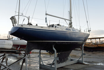 Blue sloop rigged sailboat standing on land in a yacht club. Service, repair, transportation,...