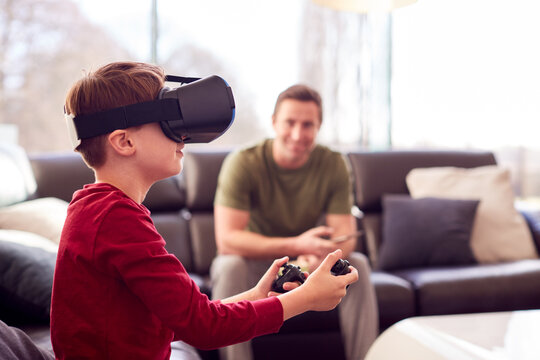 Father Watching Son Wearing Virtual Reality Headset Play Computer Game At Home