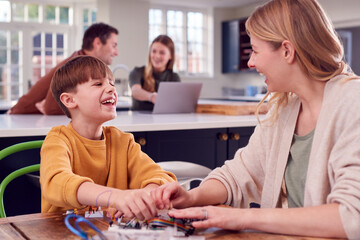 Mother Helps Son With Electronics Project Sitting At Kitchen Table At Home With Laptop