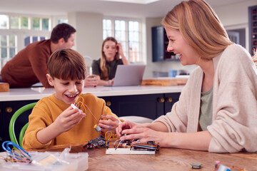 Mother Helps Son With Electronics Project Sitting At Kitchen Table At Home With Laptop