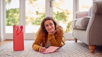 Woman In Cosy Warm Jumper Lying On Floor At Home Writing Greetings Card Or Letter