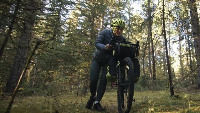 The woman travel on mixed terrain cycle touring with bike bikepacking outdoor. The traveler journey with bicycle bags. Stylish bikepacking, bike, sportswear in green black colors. Magic forest park.