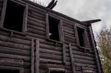 A burnt-out wooden log house against a dark gray sky. After the fire