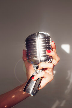 Vintage silver microphone; woman holding a mic in hand, with lens flare; isolated on gray background