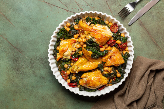 One pot chicken with kale, chickpeas and sun-dried tomatoes. Top view. Copy space, green table surface.