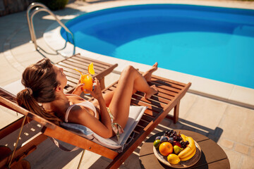 Woman drinking cocktails and sunbathing by the pool