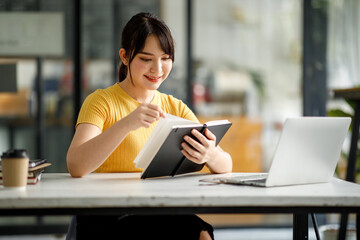 Shot of young asian female Asian young woman student sitting at table and writing on notebook. Young female student studying or reading in Coffee shop.