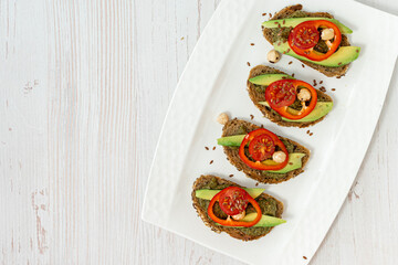 Rye bread sandwiches with vegetables and spicy sauce on a white plate and wooden table. Vegan, healthy nutrition. Diet breakfast. Top view, space for text.