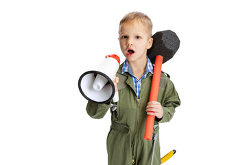 Shouting at megaphone. Little boy, cute kid in image of auto mechanic or fitter in green dungarees with work tools isolated over white studio background. Childhood, education concept