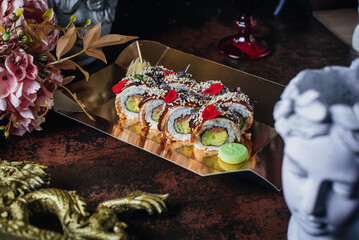 sushi in a box against the background of an ancient Greek statue and a glass of wine