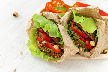 Vegan sandwiches of whole grain bread, tomatoes, peppers and avocados with spicy sauce and lettuce leaves wrapped in paper on a wooden tray. Close-up. Healthy food. Diet breakfast.