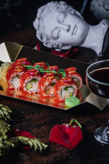 red sushi in a box against the background of an ancient Greek statue and a glass of wine
