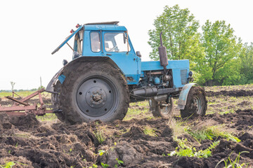Naklejka premium Old blue tractor on the field working. Farmer plowing stubble field in tractor preparing plows the land, agricultural works at farmlands, agriculture tractor-landscape. Tractor Plowing.