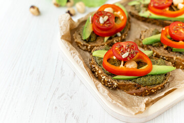 Vegan sandwiches with rye bread and vegetables on a wooden tray on a white table. A healthy breakfast or snack. Side view. Space for text. Close-up. Dietary nutrition.