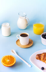 Breakfast concept with cup of coffee, croissant, milk, orange juice, yogurt and blueberries