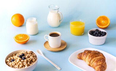 Breakfast concept with cup of coffee, croissant, wholegrain hoops, milk, orange juice, yogurt and blueberries