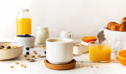 Fototapeta na wymiar Breakfast concept with cup of coffee, croissants, wholegrain hoops, milk, orange juice, yogurt and blueberries